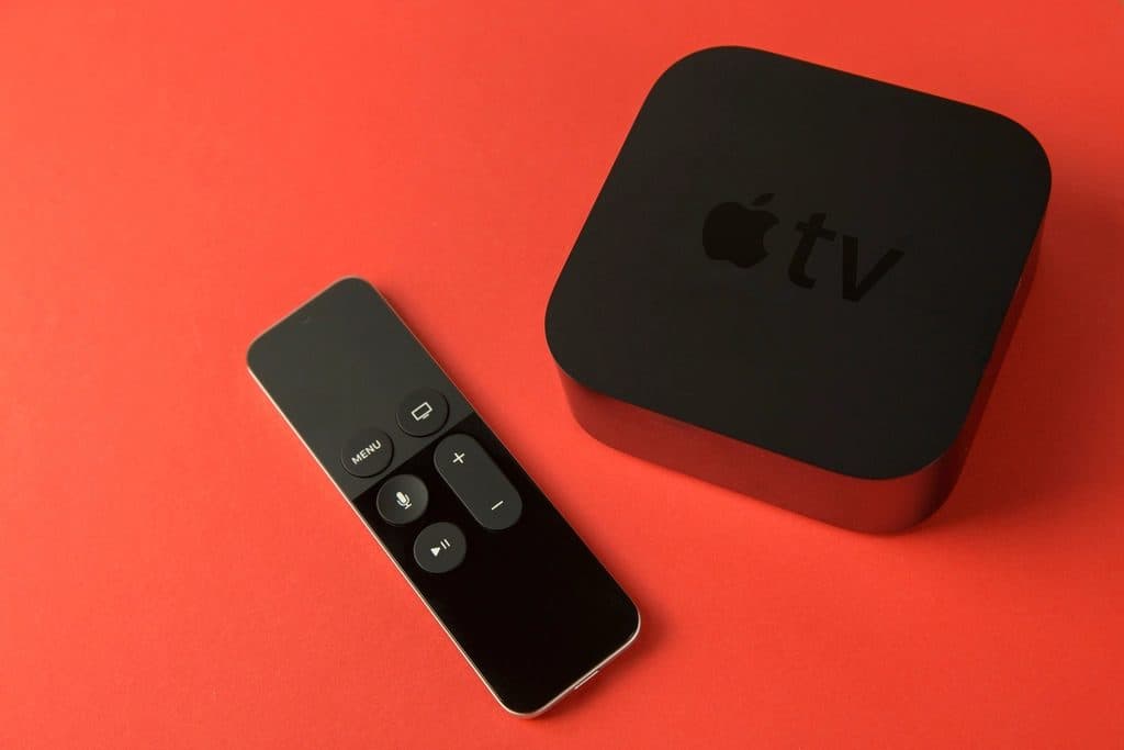 An Apple TV streaming box and its remote on a red surface